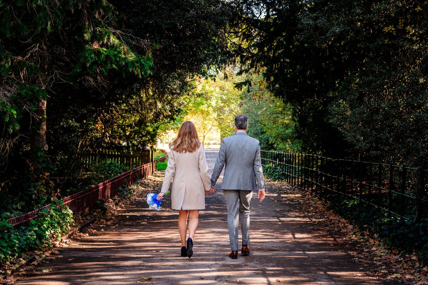 A couple walks down a tree-lined pathway in a romantic outdoor setting during golden hour lighting.
