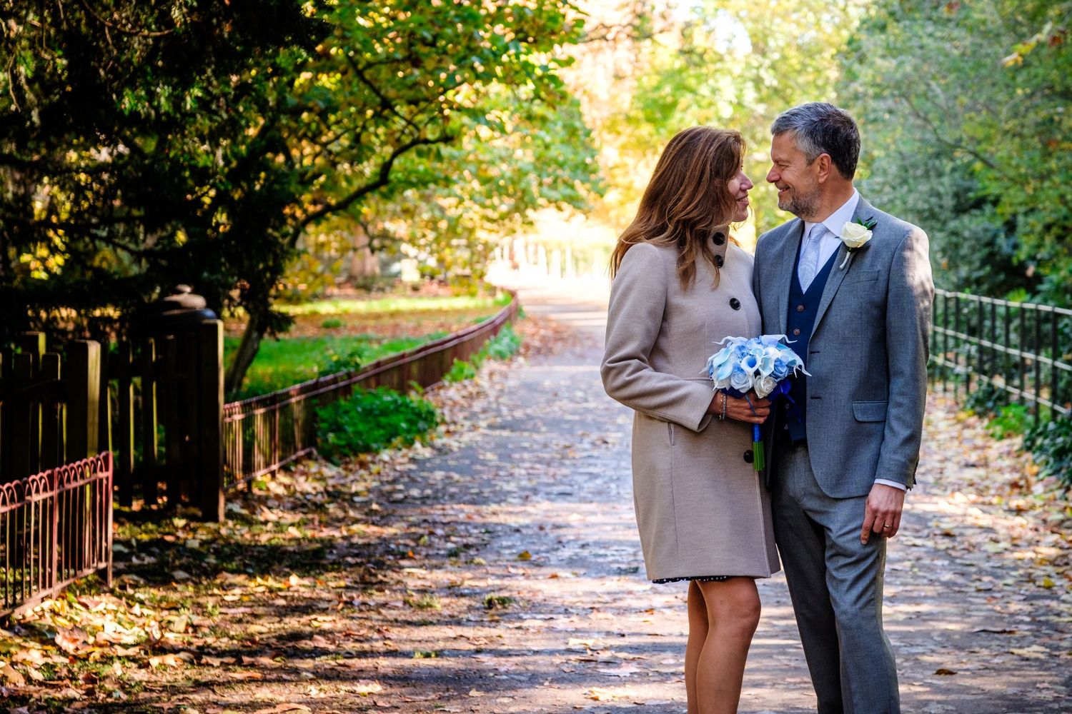 A couple shares a romantic moment walking together on a sunlit autumn path through the woods.