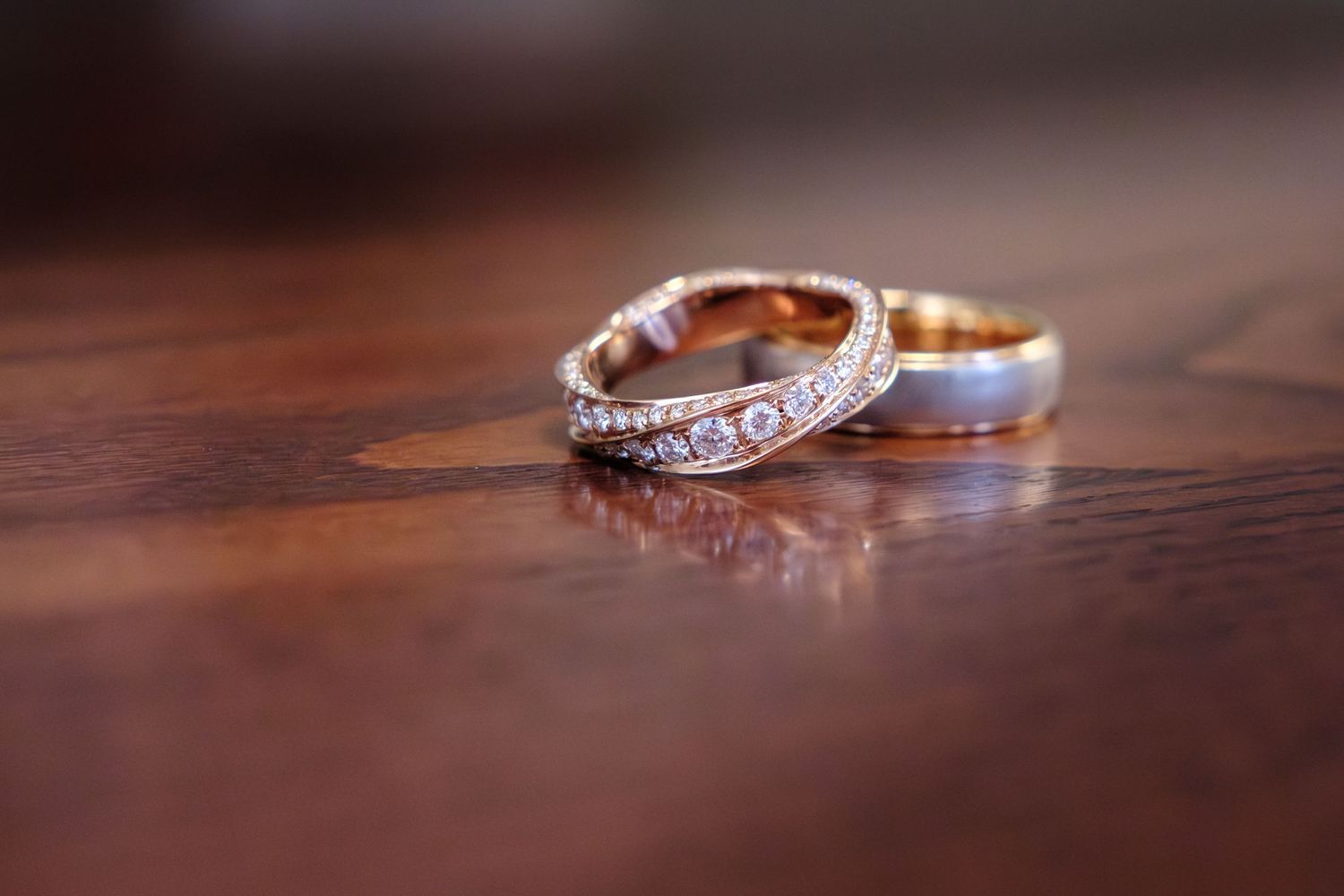 Wedding rings and engagement rings with diamonds rest on a polished wooden surface in varying angles and lighting.