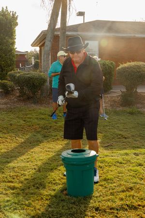 Person demonstrating golf ball cleaning technique using a green bucket washer on a sunny lawn.