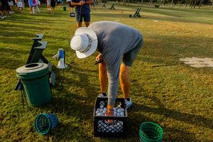 Outdoor event setup with green bins and tables arranged on grass in late afternoon light.