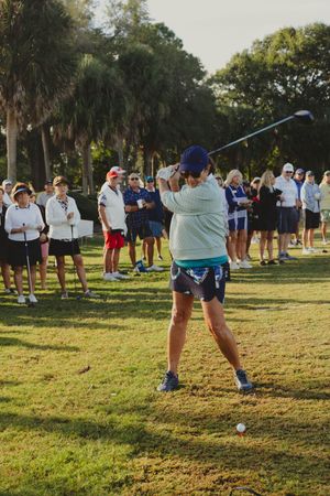 Crowd watches as golfer takes a shot during an outdoor tournament event.