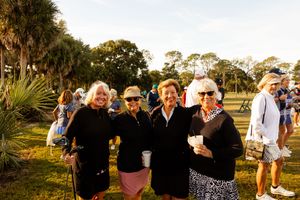 Group gathering at sunset during an outdoor golf event with palm trees in background.