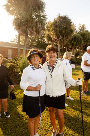 Golf event participants in matching black and white outfits posing together on grass.