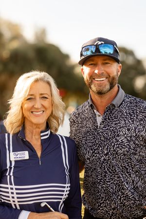 Two golfers pose together outdoors wearing athletic apparel and smiling at the camera.