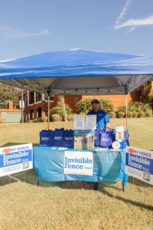 Vendor booth setup with blue canopy and Invisible Fence branded signage at outdoor event.