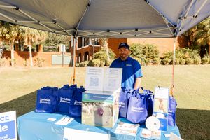 Row of blue branded display tables set up under white canopy tents at an outdoor event.