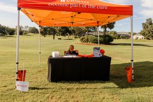 Vendor booth with orange canopy and table display set up on golf course.