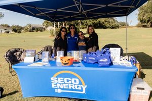 Outdoor event setup with blue branded tables and tents at a golf course on a sunny day.