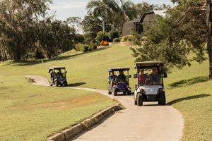 Golf carts driving along a winding path on a sunny hillside golf course.