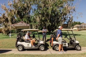 Golf carts lined up on a path with trees and grass in the background.