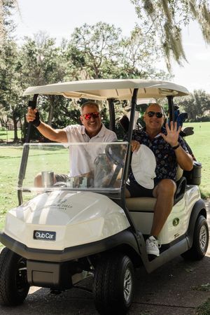 Group riding in white golf carts along a shaded path under oak trees.