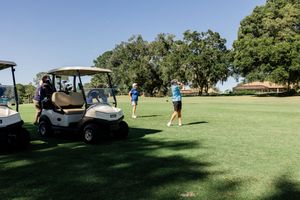 Panoramic view of a lush green golf course with scattered golf carts and players on a sunny day.