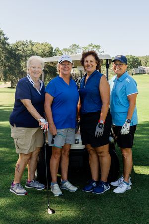 Group of golf participants posing together at a charity tournament on a sunny course.