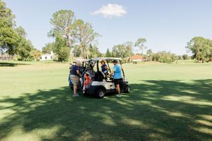 Panoramic view of a sunny golf course with golf carts and players scattered across the green landscape.