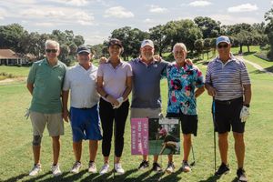 Group photo of golf tournament participants on sunny course.