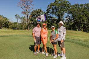 Golfers gathered on a sunny golf course with carts and trees in the background.
