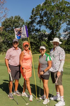 Group of golfers posing with their clubs on a sunny golf course green.