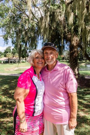 Couple wearing coordinating pink and white outfits smiling together on a sunny golf course.