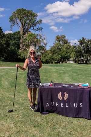 Purple banner display with Aurelius branding set up on grassy field under blue sky.