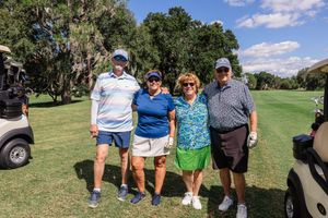 Group of people gathered on a golf course with golf carts visible in the background.