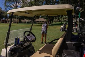 Golf cart parked on a sunny course with a player visible in the background.