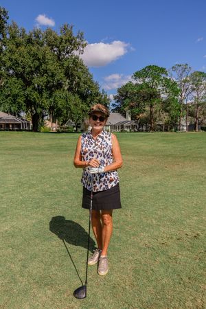 Golfer practicing their swing form on a sunny golf course with trees and houses in the background.