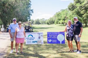 Event sponsors pose with promotional banners on golf course during tournament.