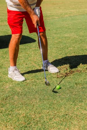 Close-up of golf club and feet positioning on green grass during a golf shot.