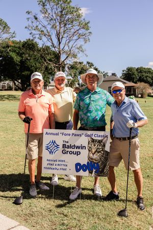 Golfers standing by tournament sponsor signs including Baldwin Group at annual golf classic.