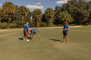 Players gathered on a sunny golf course green during a tournament.