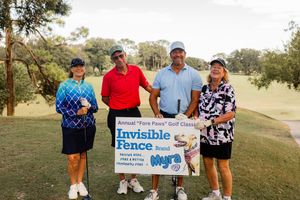 Players gathered around event signage on a golf course during a charity tournament.