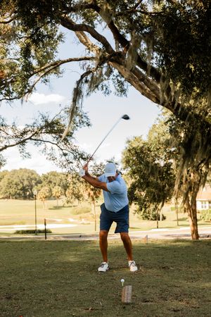 Golfer demonstrating proper form during a swing on a tree-lined course.
