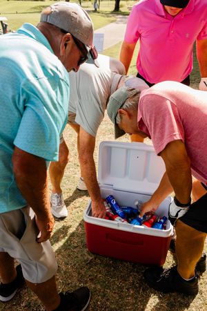 Multiple people reaching into white coolers filled with drinks and refreshments outdoors.