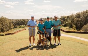A group of people posing together on a sunny golf course with rolling hills and trees in the background.