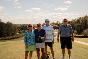 Panoramic view of golfers gathered on a sunny golf course with trees in the background.