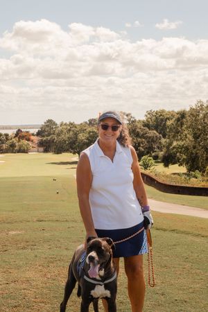 Person walking with a black and white dog on a scenic golf course path.