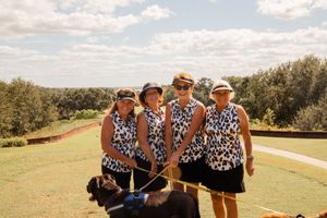 A group wearing matching patterned outfits poses together on a grassy hill under blue skies.