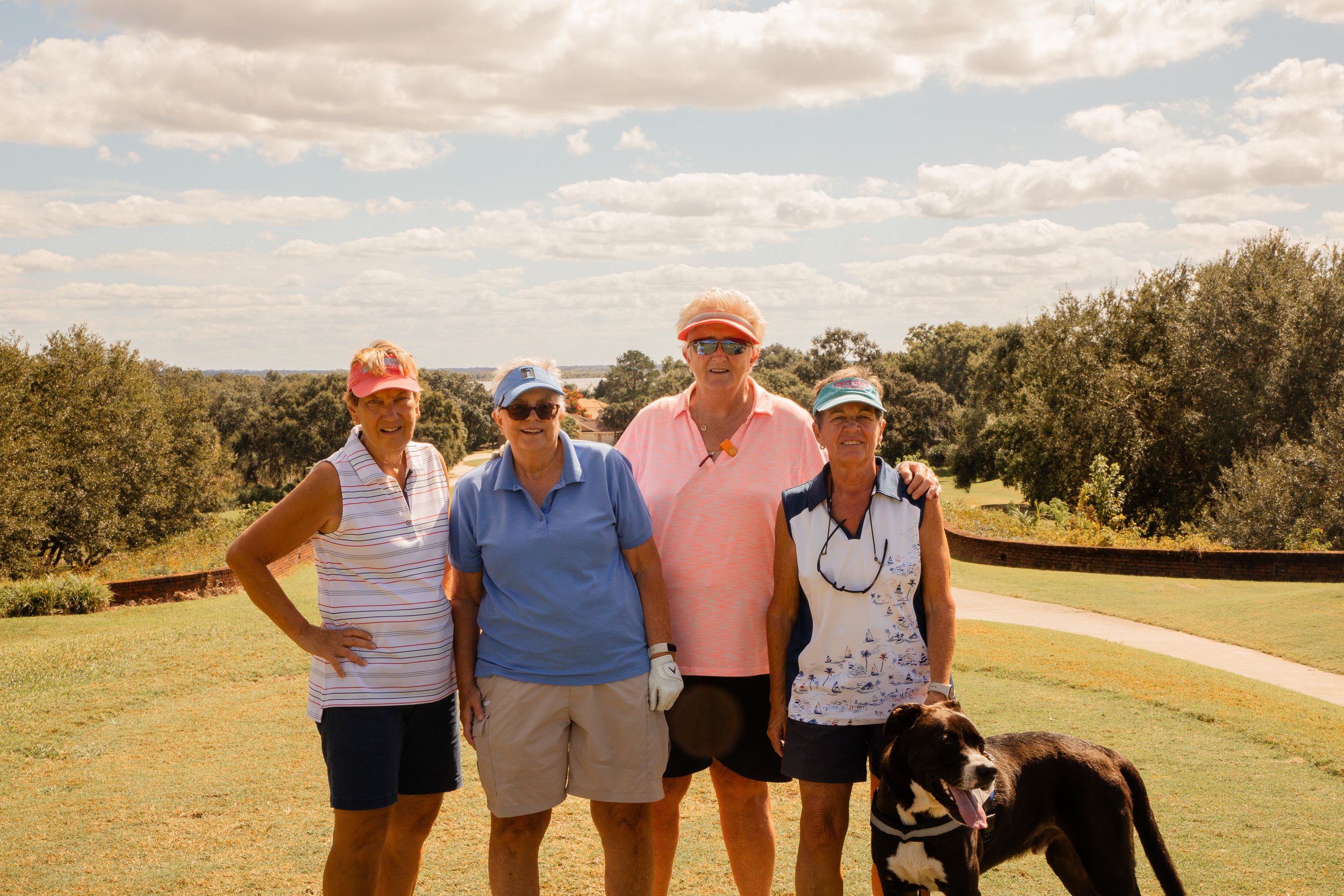 Golfers standing together on a scenic golf course under partly cloudy skies.