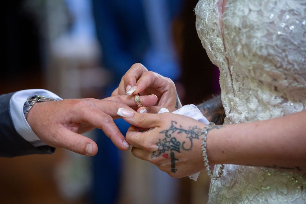 Close-up of bride placing wedding ring on grooms tattooed hand during ceremony.