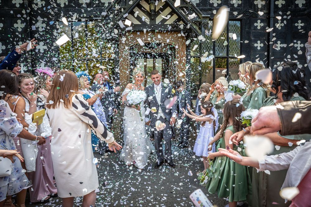 Newlyweds exit church through a joyful shower of white confetti with cheering guests.