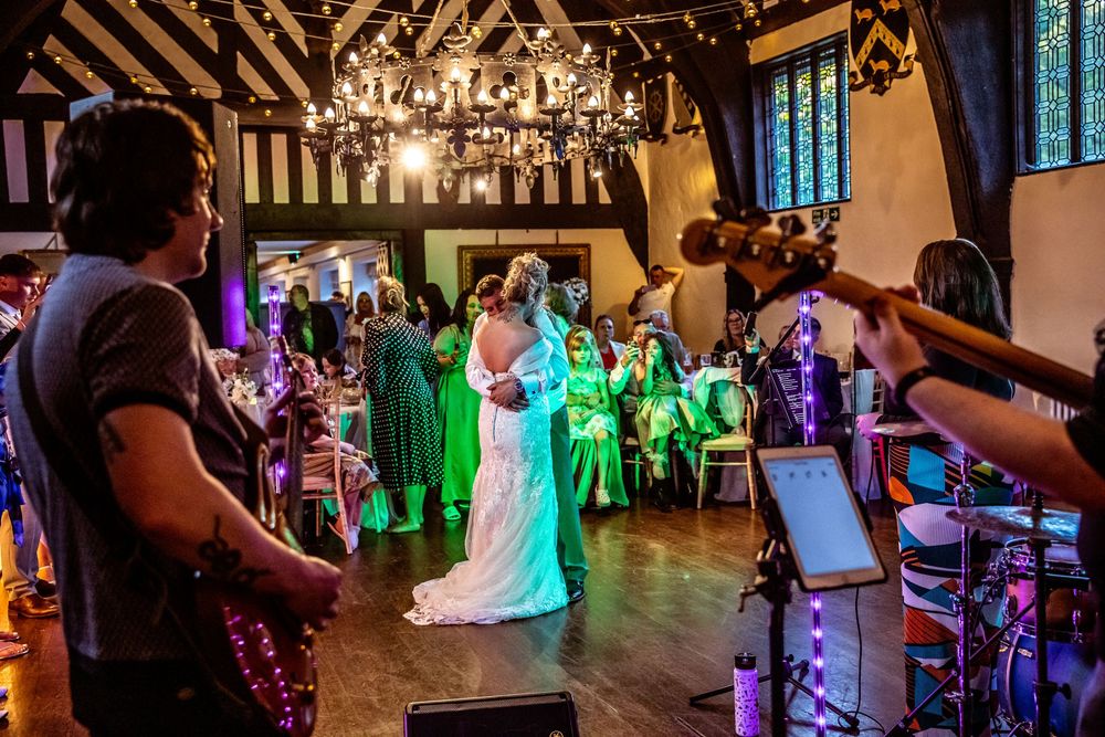 Bride and groom share their first dance in a rustic wedding venue with live band and colorful lighting.