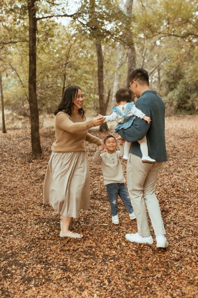 A family plays together on fallen autumn leaves in a wooded area during a fall photo session.