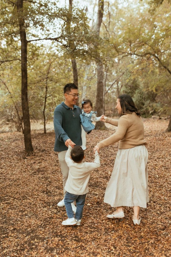 A family plays together on fallen autumn leaves in a wooded area during a warm fall day.