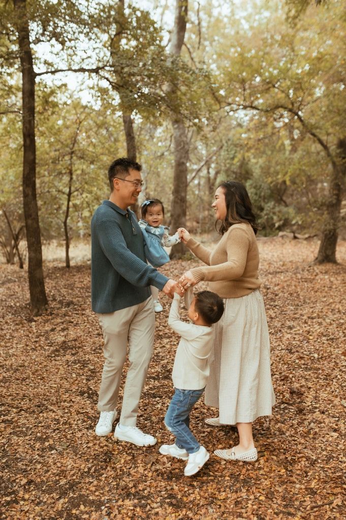 A family shares a tender moment together while standing on fallen leaves in a forest setting.