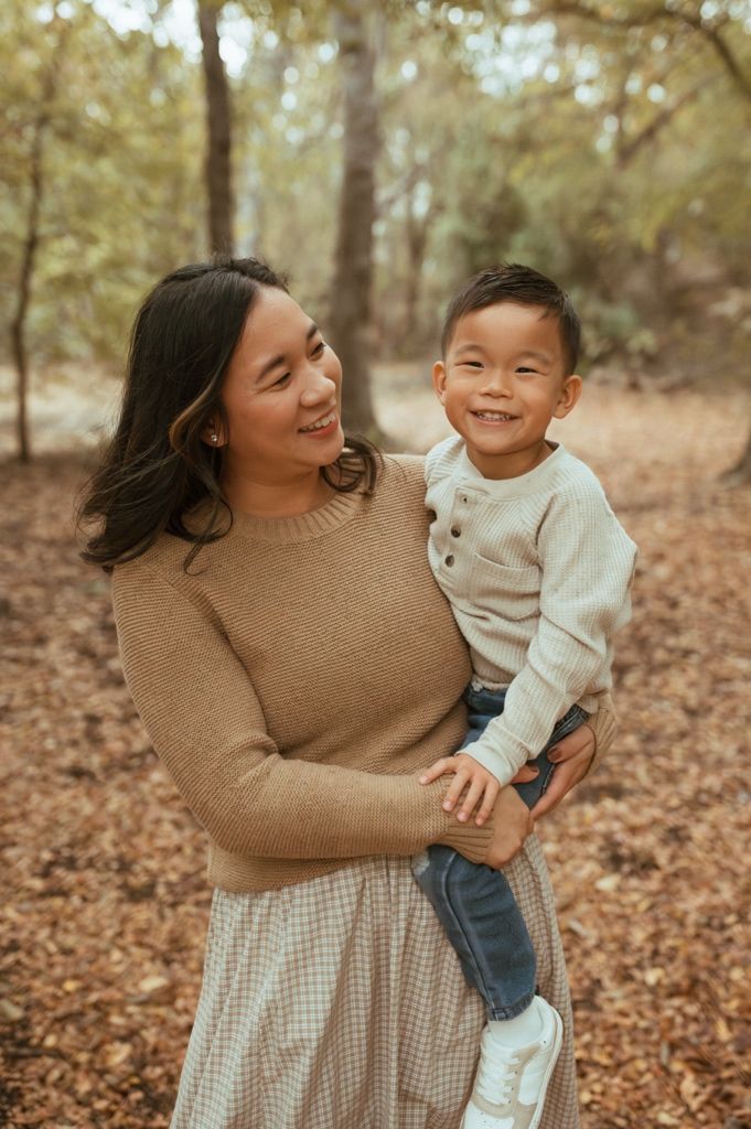 Joyful moments shared between parent and child playing in a wooded area with fallen leaves.