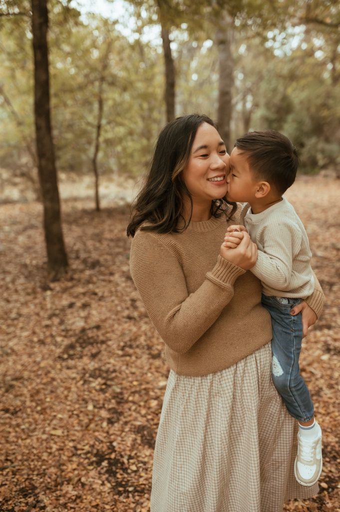 A heartwarming moment of affection captured between parent and child in an autumn forest setting.