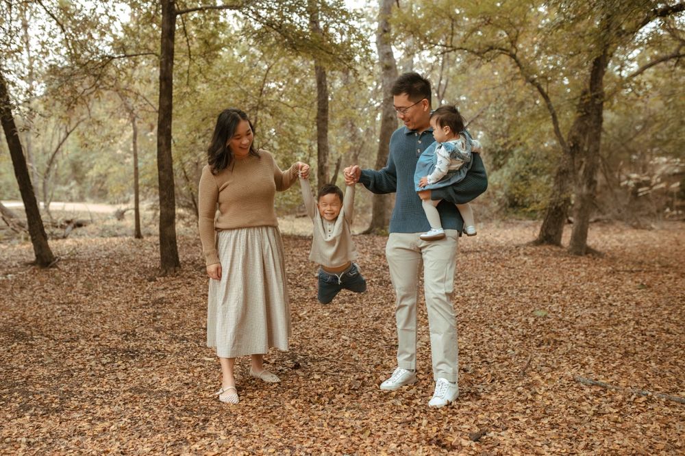 A family enjoys a playful autumn day together in a wooded park with fallen leaves.
