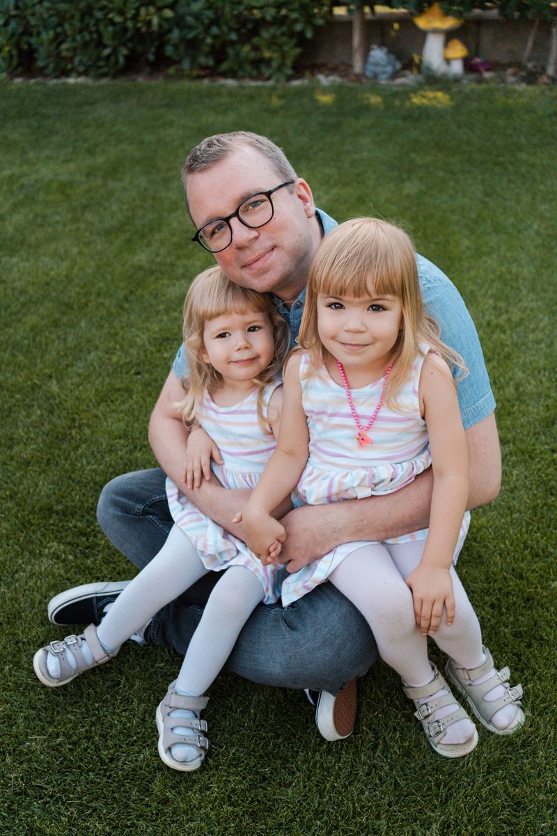 outdoor photos showing parent and two young children sitting together on grass in matching outfits during a family photoshoot in Rouse Hill