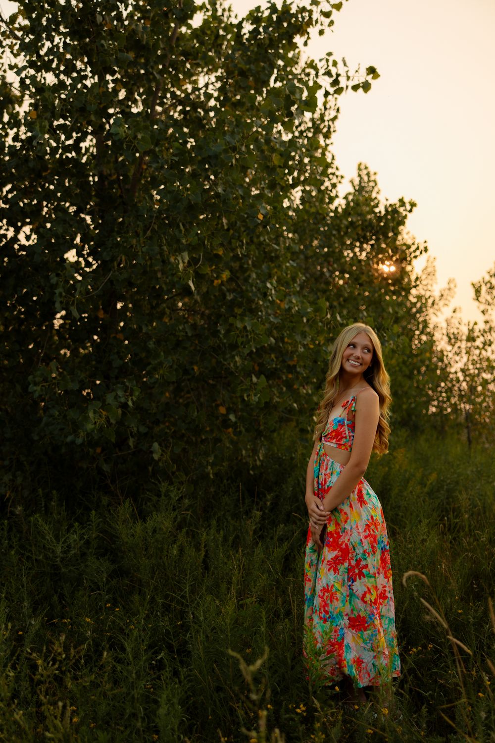 A colorful floral dress catches the golden sunset light among lush greenery in an outdoor garden setting.